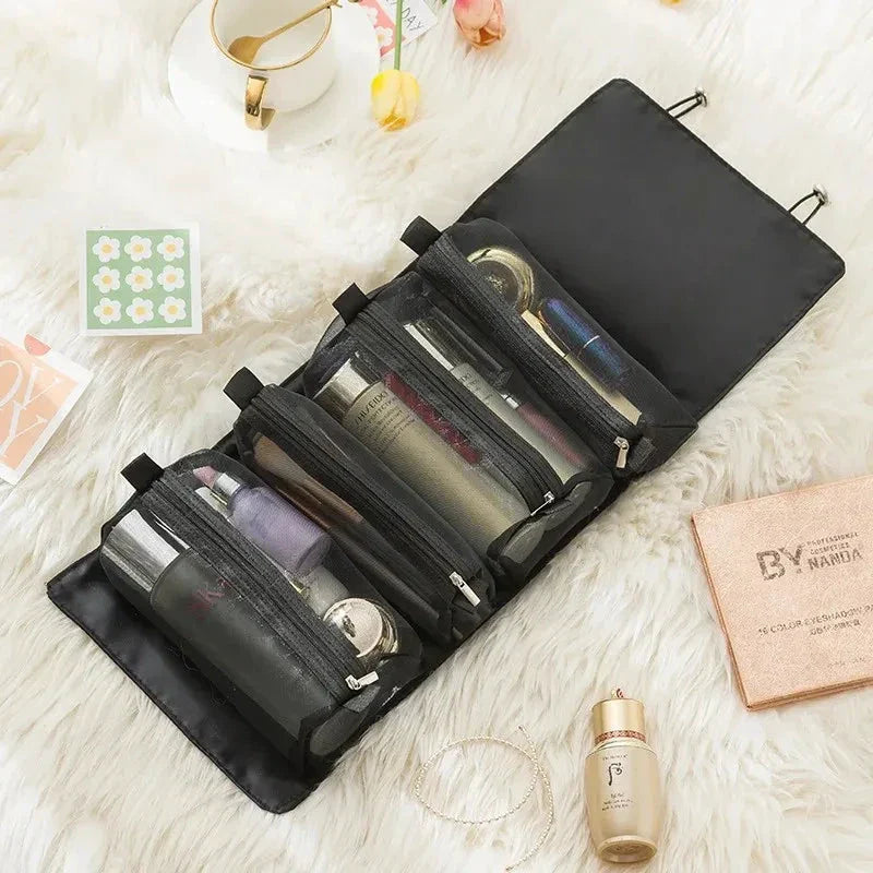 Black travel organizer bag with four expanded compartments holding personal items on a bed.
